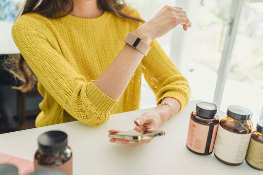 Woman checking fitness tracker and holding phone at home
