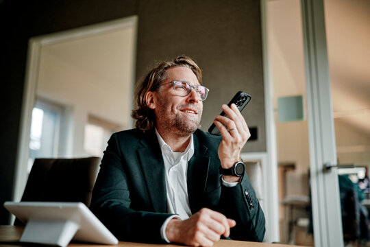 A smiling businessman talks on a smartphone at the office desk