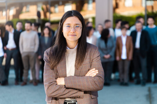Smiling businesswoman crosses arms outdoors with team in background
