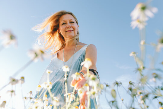 Smiling woman reaches for chamomile flower outside in summer