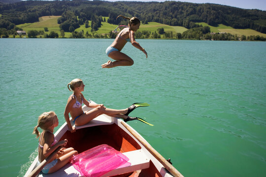 Girls (8-15) sitting on boat, one jumping in water, side view