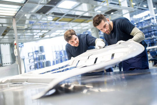 Two colleagues examining component in car factory