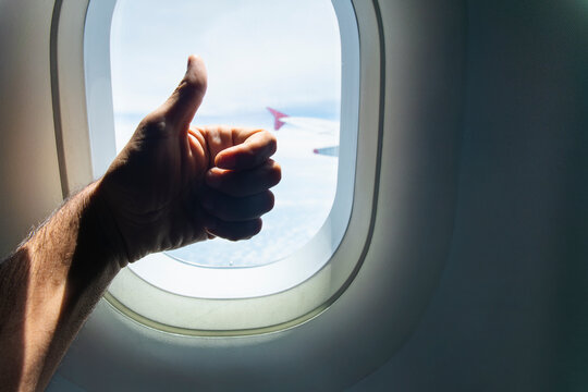 Male passenger shows approval near an airplane window during flight