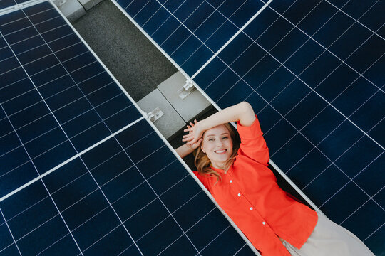 A smiling woman lies between solar panels to support green energy
