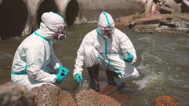Two environmental workers collecting and examining wastewater sample, water quality testing, pollution monitoring, contamination analysis, environmental fieldwork.