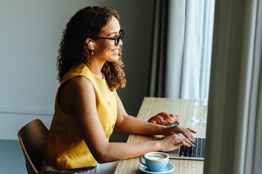 Mixed-race woman typing on laptop during a remote meeting at home office desk