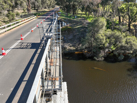 Scaffolding installed on a rural bridge to provide safe access for maintenance and inspection work. Metal platforms and supports surround the bridge structure over a small waterway.