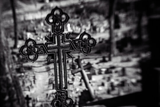 Old iron cross in cemetery. Black and white image. Selective focus, tilt shift, partly blurred. Ancient tombstone detail.