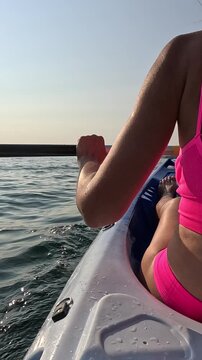 Woman kayaking across glistening ocean waters in a pink swimsuit while moving toward the horizon. Handheld rear-view shot.