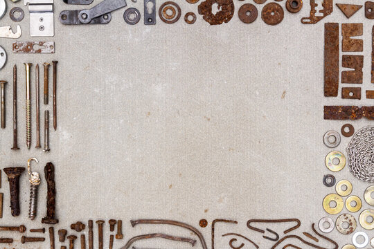 A frame of various old rusty bits and pieces arranged on a concrete surface. Old rusty nuts, bolts, nails and other parts flay lay on gray background.