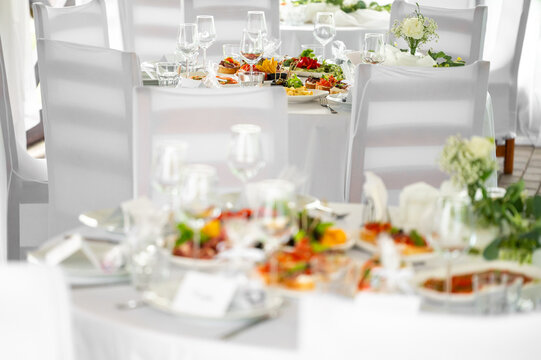 White banquet tables with appetizers and wine glasses ready for a wedding or corporate event in a restaurant.