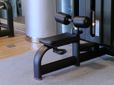 Modern Black Lat Pulldown Machine with Padded Seat and Leg Rollers Close Up View of Professional Weight Stack Cable Equipment in Modern Gym Interior
