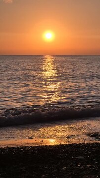Golden sunset ocean view with waves washing onto a pebbled shoreline during peaceful evening. Stationary shot.