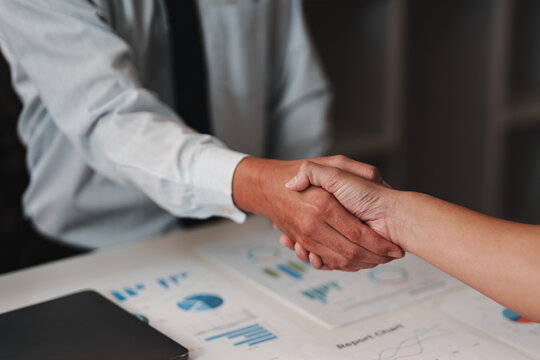 Business handshake over financial charts and investment report in modern office