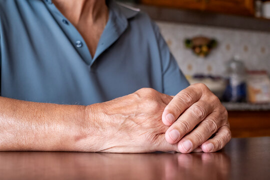 Senior person resting hands on a wooden table, displaying the visible signs of aging with wrinkles and veins, conveying concepts of wisdom, experience, and the passage of time