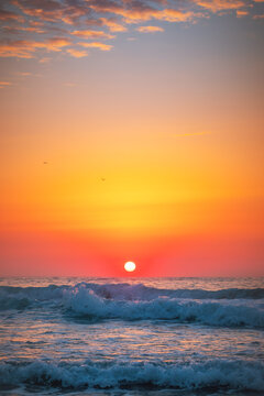 Vertical shot of vibrant red sun rising over crashing ocean waves