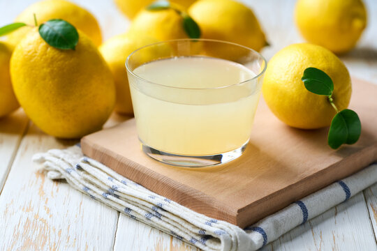 Freshly squeezed lemon juice in a glass with halved lemons on white table, selective focus. Organic lemon juice in a glass on table