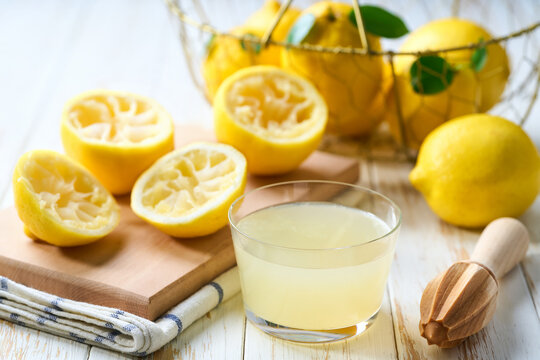 homemade lemon juice in a glass on table. Freshly squeezed lemon juice in a glass with halved lemons on white table, selective focus.