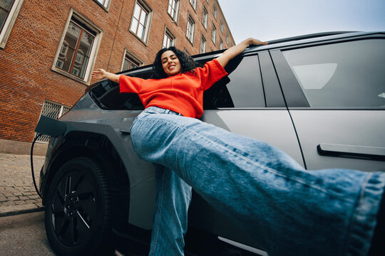 Standing by the car, the woman pauses on a city street while her car charges
