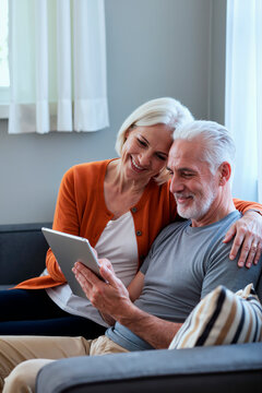 Vertical shot of senior Caucasian couple using tablet together, reviewing online content at home and sharing digital lifestyle moment. Ideal for retirement planning, telehealth, ecommerce