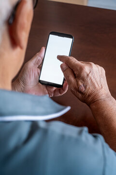 Senior person hands holding a modern smartphone with a blank white screen, actively tapping the display, symbolizing elderly engagement with digital technology and communication