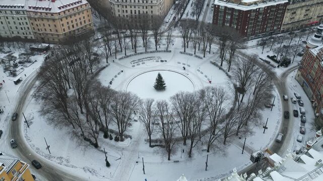 Stockholm, Sweden, Drone Shot of Snow Capped Circular Karlaplan Park on Winter Day, Roundabout Traffic and Buildings