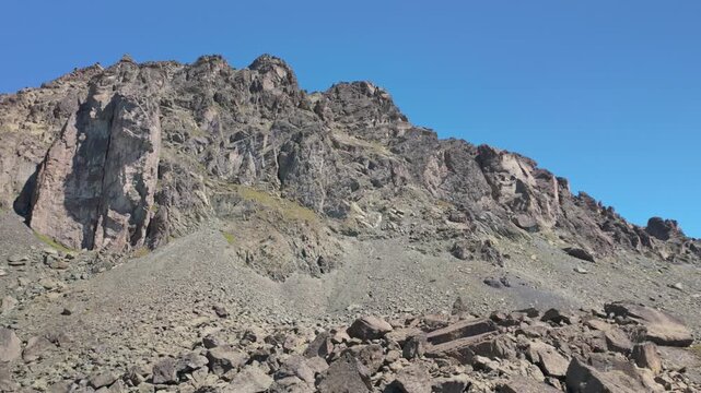 Rugged volcanic mountain ridge with exposed rock, loose scree, and a clear blue sky in a stark alpine landscape of Silvretta. Motion right.
