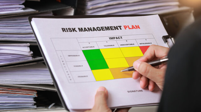 Focused executive holding pen in hand to review risk management plan document on clipboard for corporate office analysis