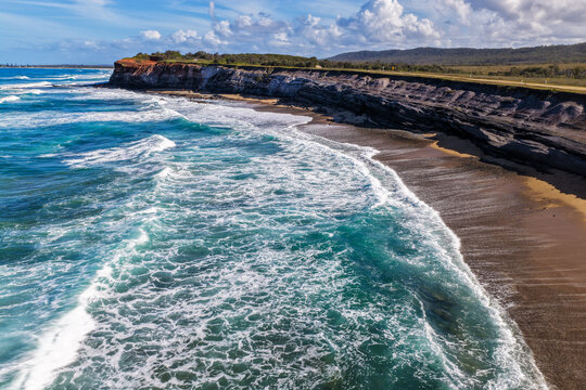Aerial view of the rugged rocky cliffs and sandy shoreline of Lake Arragan Beach, featuring the Pacific Ocean, exposed coastal rock formations and natural bushland within Yuraygir National Park 