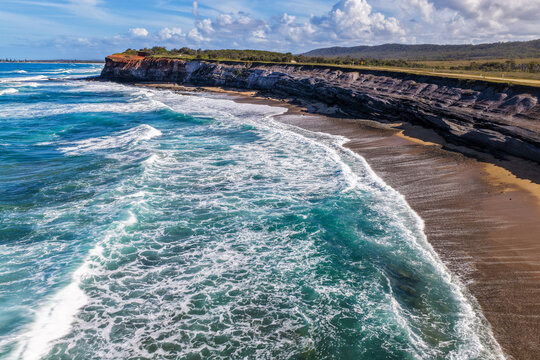 Aerial view of the rugged rocky cliffs and sandy shoreline of Lake Arragan Beach, featuring the Pacific Ocean, exposed coastal rock formations and natural bushland within Yuraygir National Park