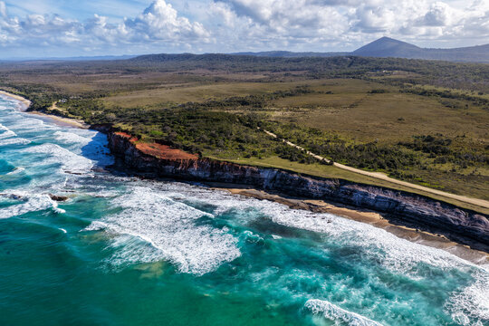 Aerial view of the rugged rocky cliffs and sandy shoreline of Lake Arragan Beach, featuring the Pacific Ocean, exposed coastal rock formations and natural bushland within Yuraygir National Park