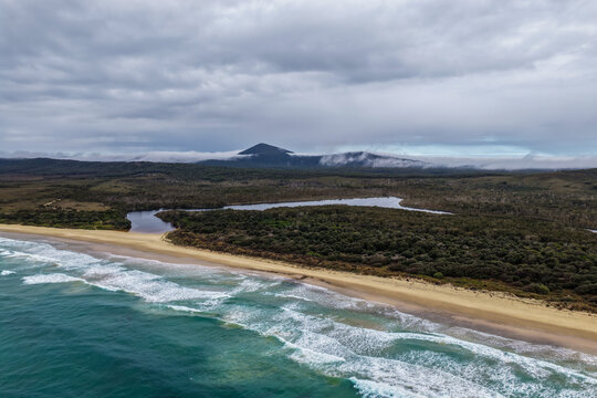 Aerial view of Lake Arragan Beach and the surrounding coastal landscape, featuring a long sandy shoreline, Pacific Ocean, native bushland and pristine natural scenery within Yuraygir National Park