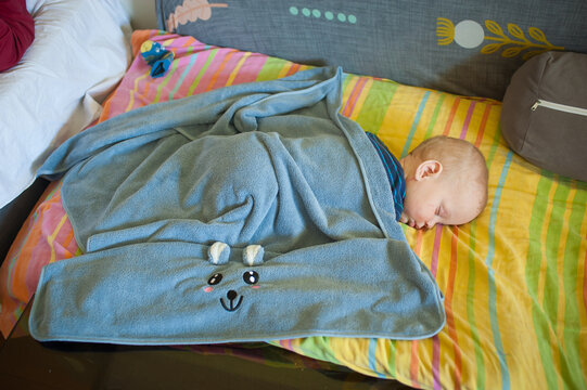 A sleeping infant rests under a soft blue animal-themed blanket during a quiet, peaceful morning nap