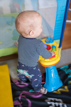 Curious baby boy standing upright and exploring a colorful musical activity table in his nursery during a bright and sunny afternoon at home