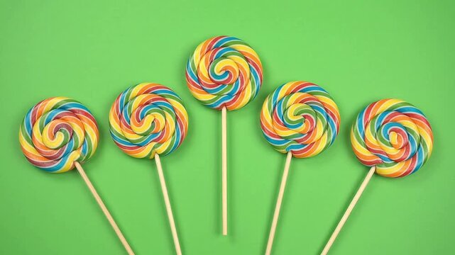 Colorful swirl lollipops rotating on sticks over green background