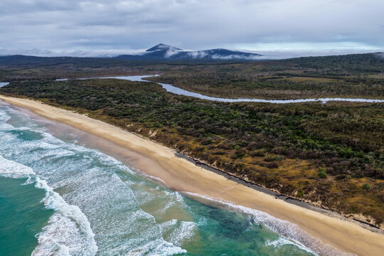 Aerial view of Lake Arragan Beach and the surrounding coastal landscape, featuring a long sandy shoreline, Pacific Ocean, native bushland and pristine natural scenery within Yuraygir National Park