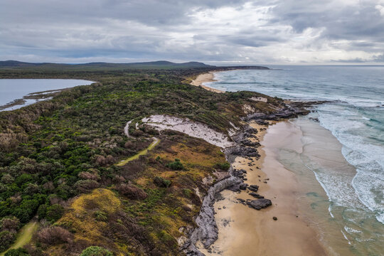 Aerial view of Lake Arragan Beach and Lake Arragan within Yuraygir National Park, showcasing the sandy Pacific coastline, coastal lake, native bushland and surrounding natural landscape 