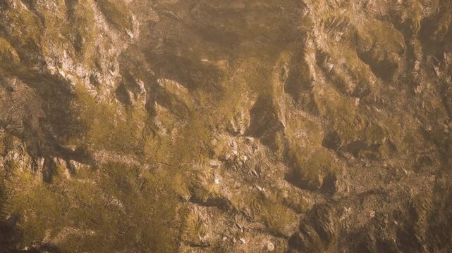 The scene shows rocky terrain with various textures and colors under bright light. The view captures the natural landscape featuring steep and flat areas.