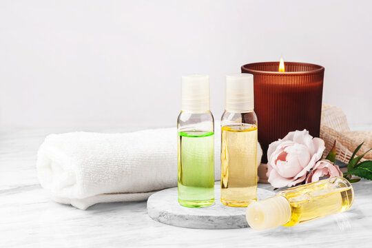 Cosmetic beauty bottles with burning aroma candle, towel and pink roses on marble table, spa and wellness background