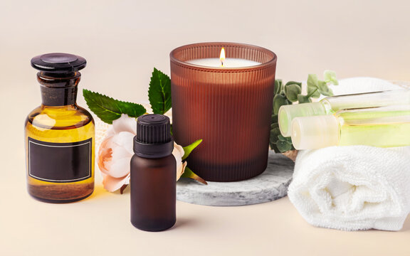 Spa concept with scented candle, essential oil bottles and towel with flower on beige background