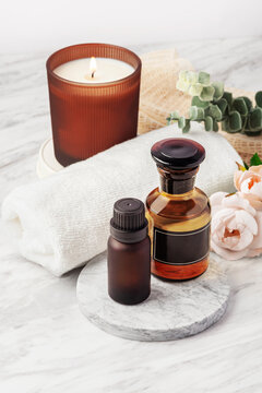 Spa essential oil bottles and scented candle on marble table with towel and green leaves decoration