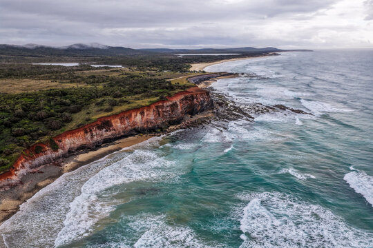 Aerial view of the rugged rocky coastline and coastal cliffs at Lake Arragan, featuring exposed rock formations, Pacific Ocean and surrounding native landscape within Yuraygir National Park