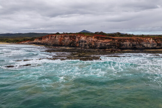 Aerial view of the rugged rocky coastline and coastal cliffs at Lake Arragan, featuring exposed rock formations, Pacific Ocean and surrounding native landscape within Yuraygir National Park 