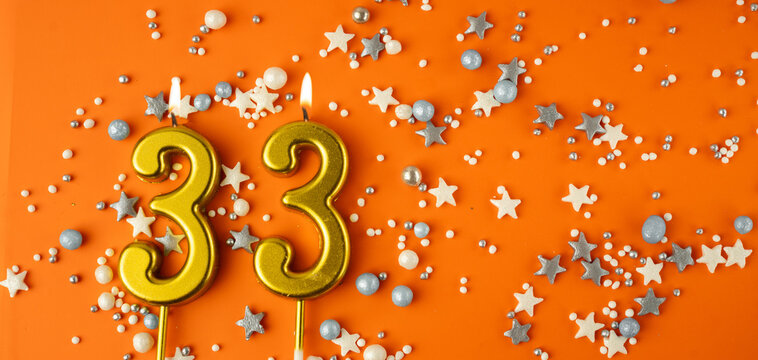 Birthday or anniversary celebration concept. Candles in the shape of the number thirty-three on an orange background among decorative ornaments. 33rd anniversary. Banner