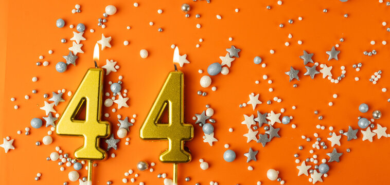 Birthday or anniversary celebration concept. Candles in the shape of the number forty-four on an orange background among decorative ornaments. 44th anniversary. Banner