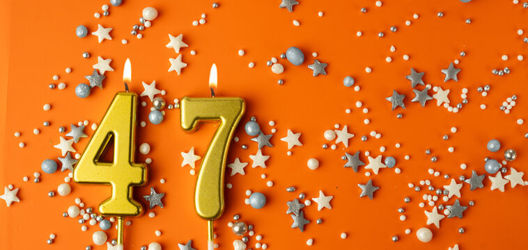 Birthday or anniversary celebration concept. Candles in the shape of the number forty-seven on an orange background among decorative ornaments. 47th anniversary. Banner