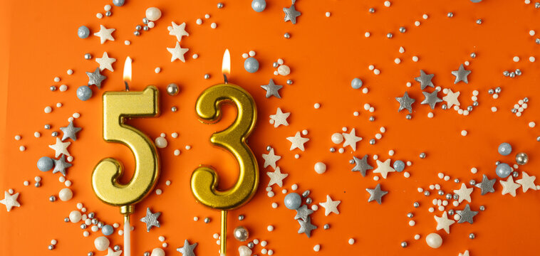 Birthday or anniversary celebration concept. Candles in the shape of the number fifty-three on an orange background among decorative ornaments. 53rd anniversary. Banner