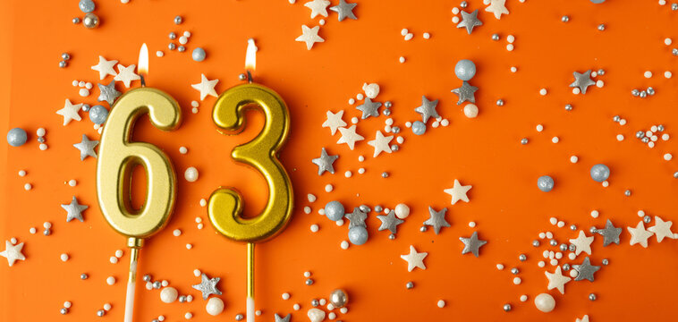 Birthday or anniversary celebration concept. Candles in the shape of the number sixty-three on an orange background among decorative ornaments. 63rd anniversary. Banner
