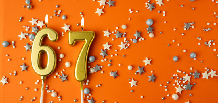 Birthday or anniversary celebration concept. Candles in the shape of the number sixty-seven on an orange background among decorative ornaments. 67th anniversary. Banner