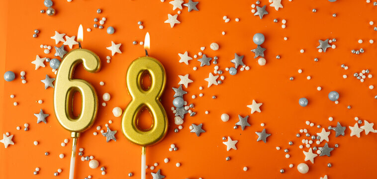 Birthday or anniversary celebration concept. Candles in the shape of the number sixty-eight on an orange background among decorative ornaments. 68th anniversary. Banner